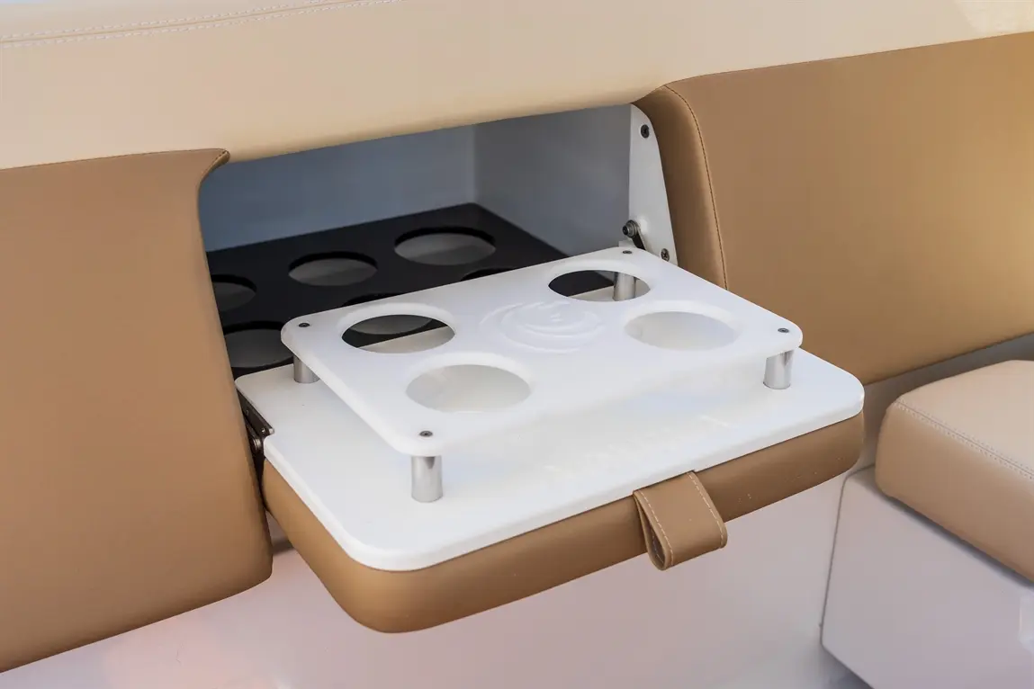 A white drink holder with four circular cutouts is mounted on tan cushioned seating in a boat, enhancing convenience.